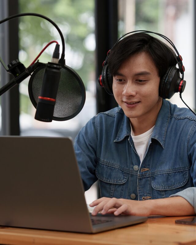 Podcast host recording an episode with headphones and a microphone at a laptop